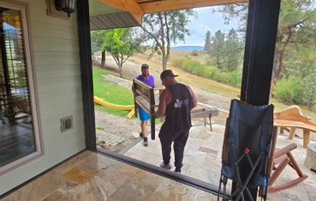 ID-Best-Moving-Company-furniture Two movers carrying a wooden furniture piece across a patio
